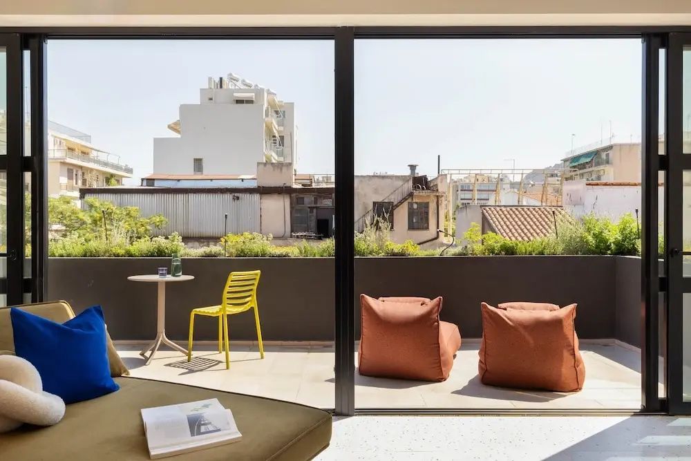 Blick durch das Fenster auf die Terrasse mit Sitzgelegenheiten und Stadtlandschaft.