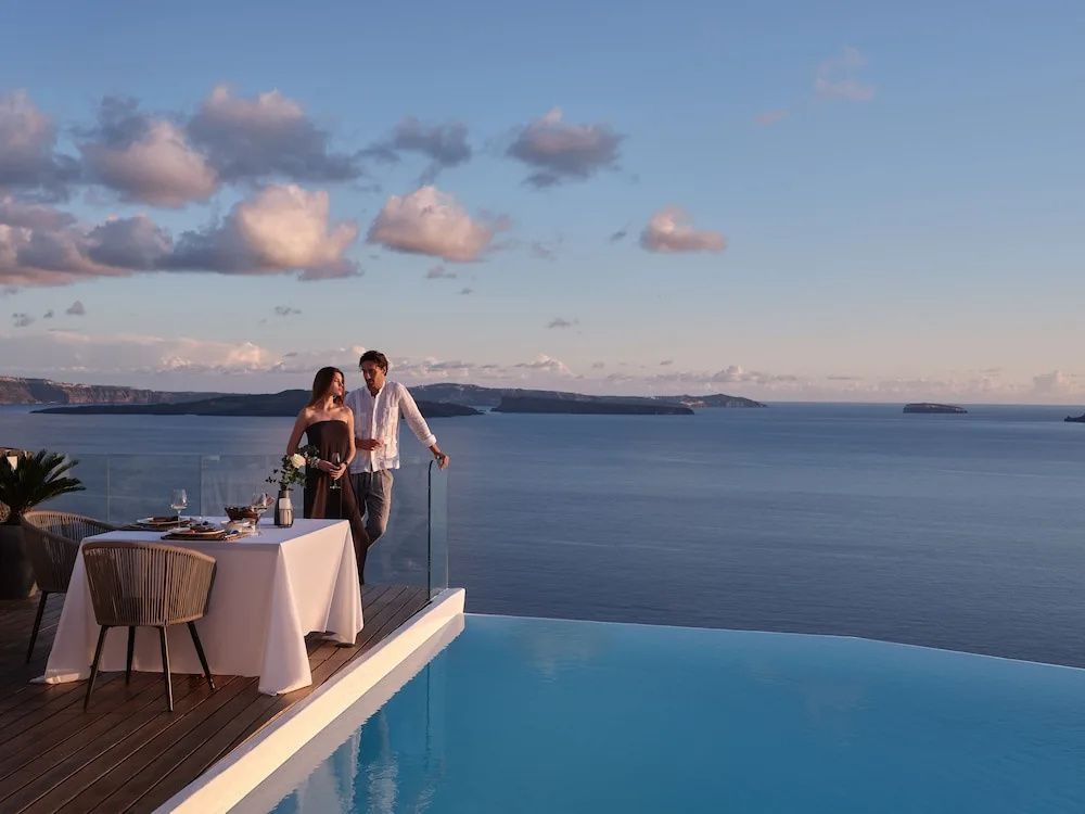 Paar auf einer Terrasse am Infinitypool mit Blick über das Meer bei Dämmerung.