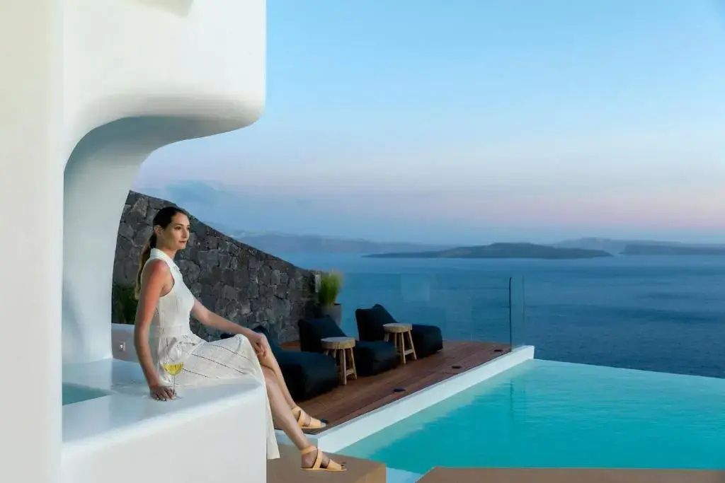 Frau sitzt auf einer weißen Terrasse mit Blick auf den Pool und das weitläufige Meer.