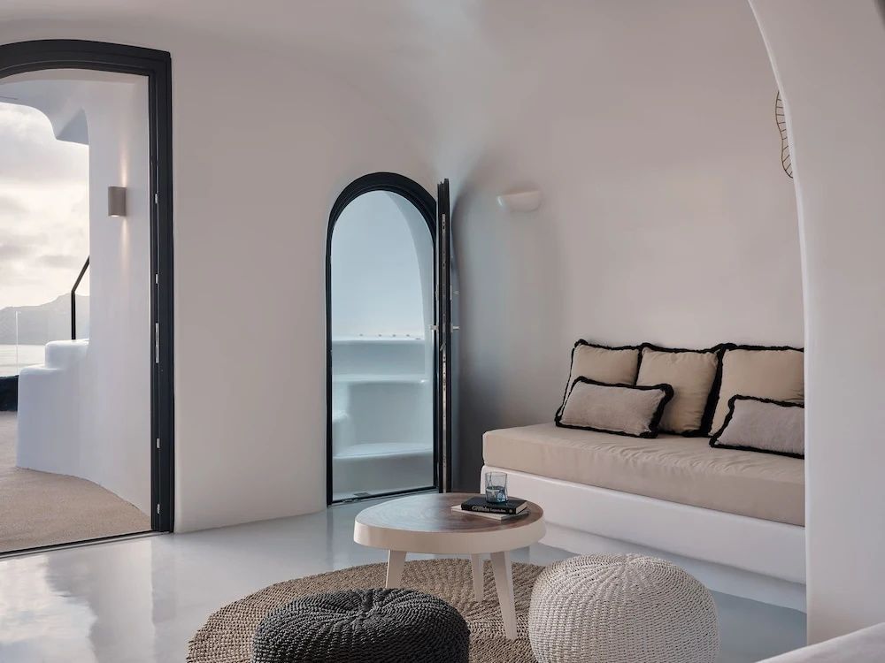 Helles Wohnzimmer mit beigem Sofa, Poufs, Teppich und rundem Durchgang.