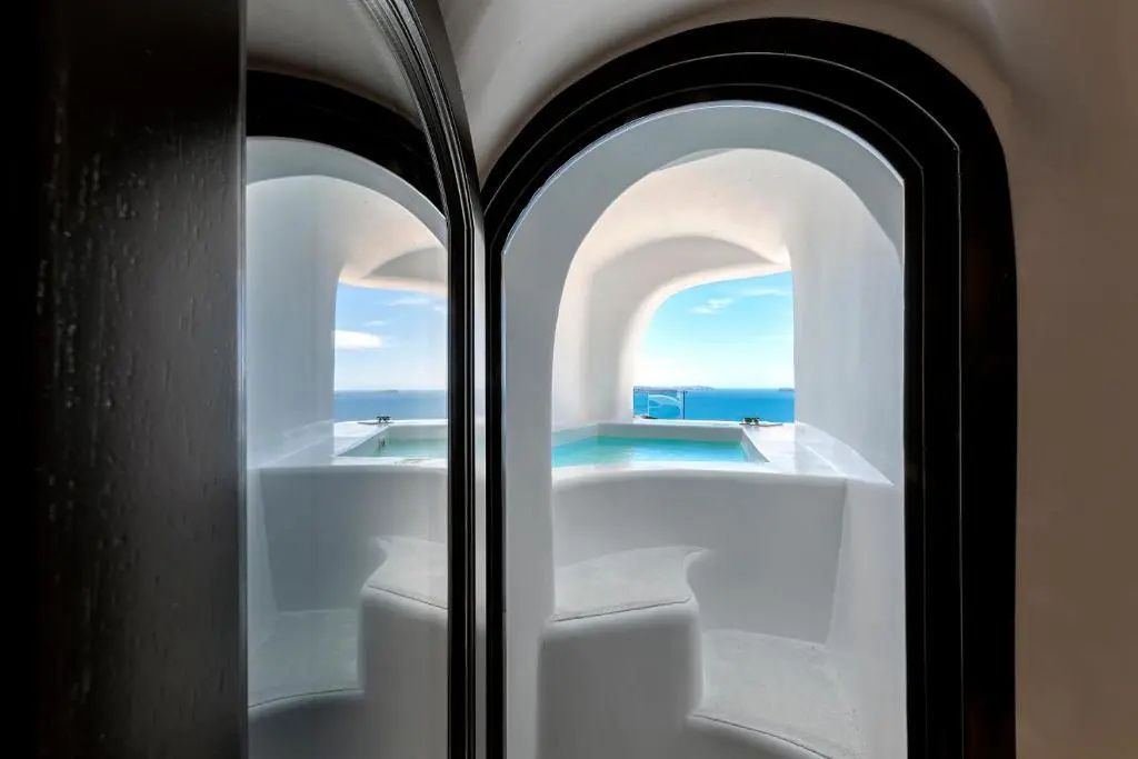 Blick durch einen weißen Rundbogen auf einen kleinen Pool und das dahinterliegende Meer.