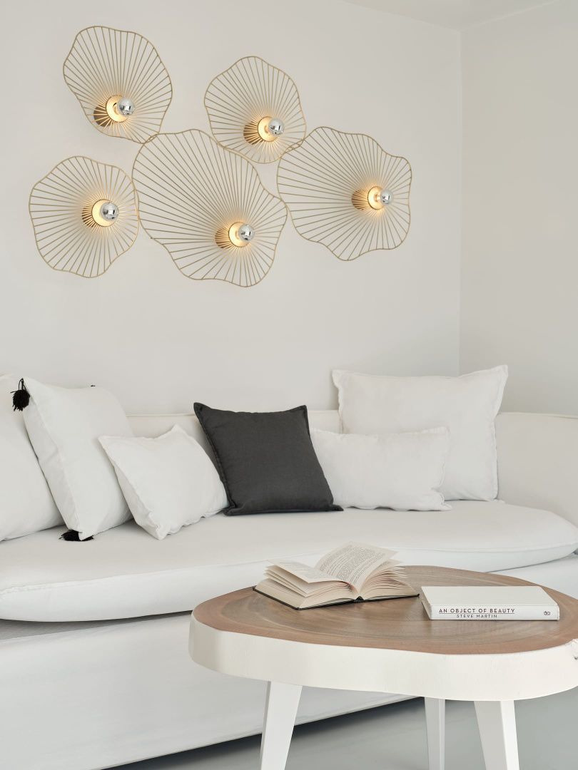 Weißes Sofa mit Kissen und blattförmigen Wandleuchten über einem Holztisch mit Büchern.