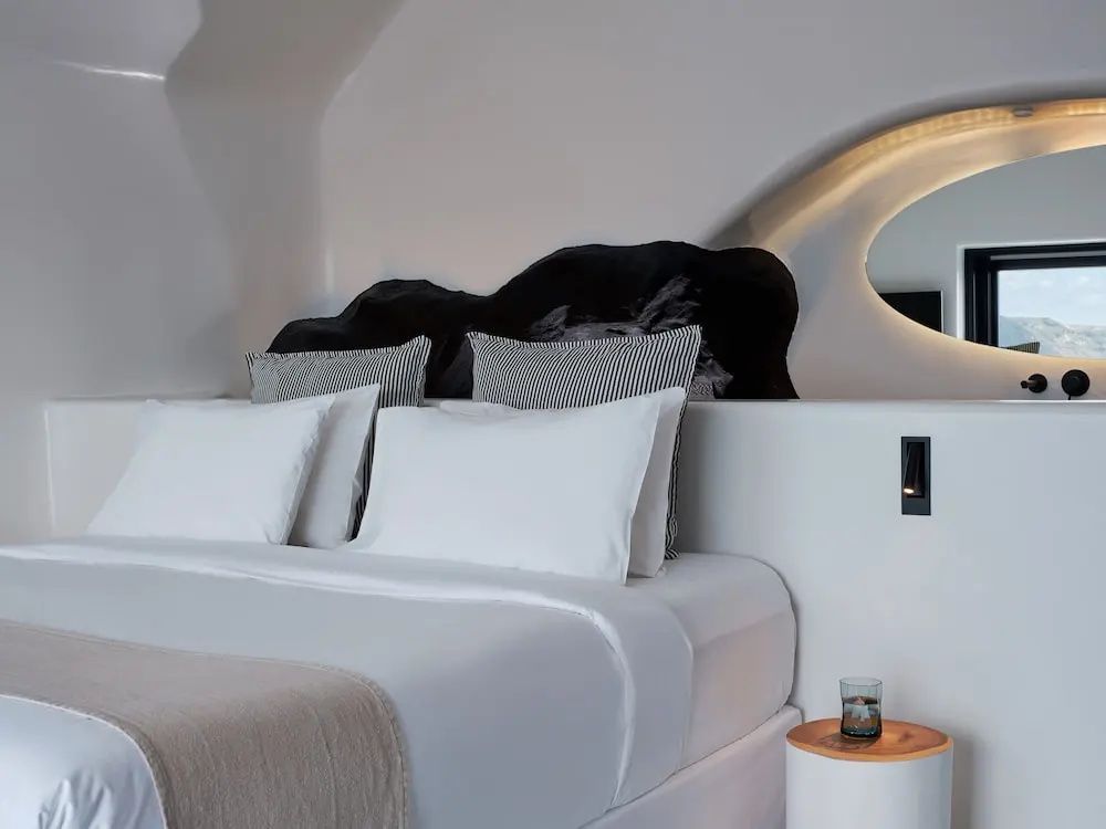 Doppelbett mit weißer Bettwäsche vor einer dunklen Natursteinwand im Zimmer.
