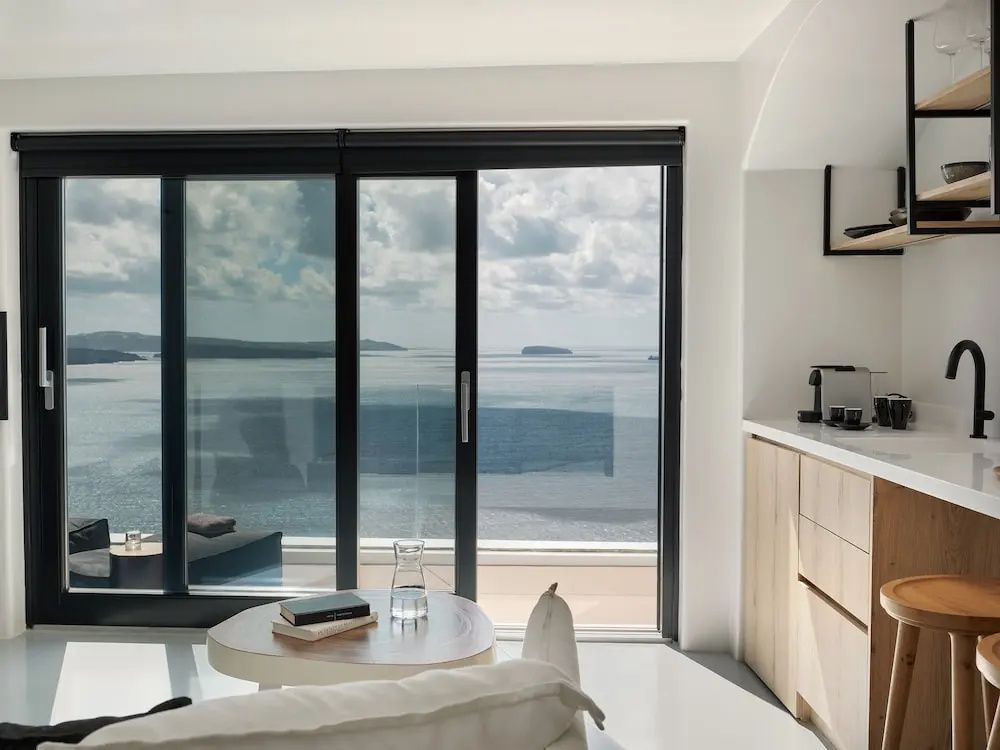 Blick durch eine große Glasfront aus dem Raum auf das Meer und weit entfernte Inseln am Horizont.