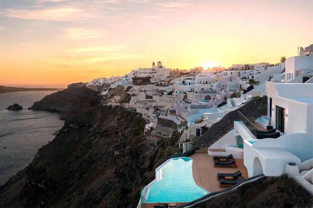 Sonnenuntergang über weiß gekalkten Häusern am Hang mit Blick auf den Infinitypool und das Meer.