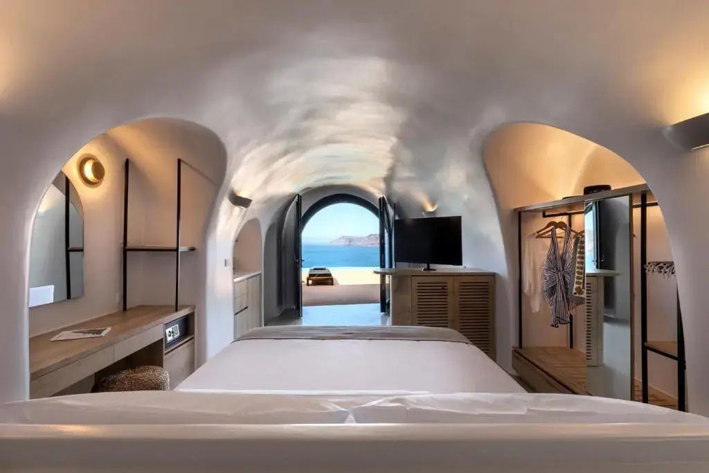 Schlafzimmer im Höhlenstil mit Doppelbett und Blick durch den Bogen auf das Meer.