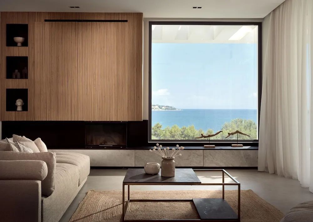 Modernes Wohnzimmer mit Sitzmöbeln und einem großen Fenster mit Blick auf das Meer.