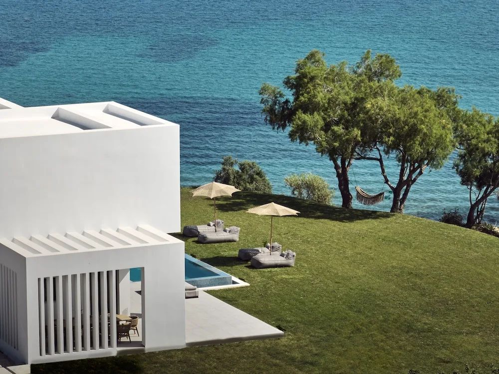 Moderne weiße Gebäudearchitektur am Meer mit grünem Garten und Liegestühlen.