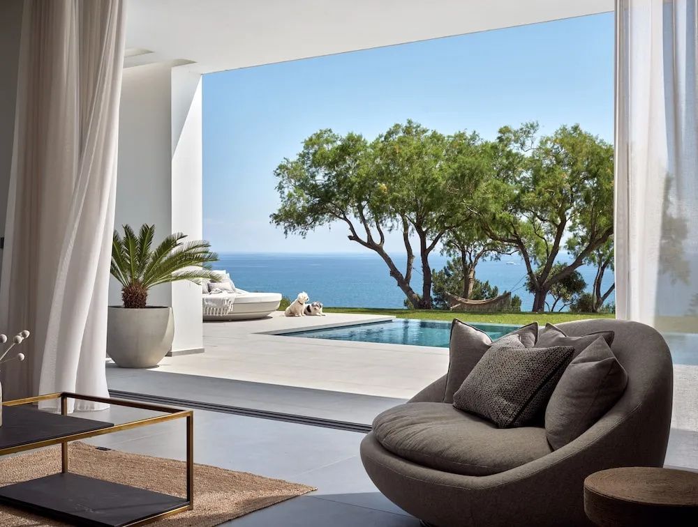 Überdachte Terrasse mit Sitzmöbeln, Blick auf den Pool, Bäume und das Meer.
