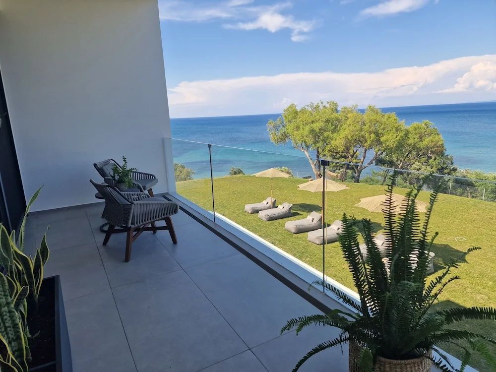 Balkon mit zwei Sesselstühlen und Aussicht auf die Liegewiese und das Meer.