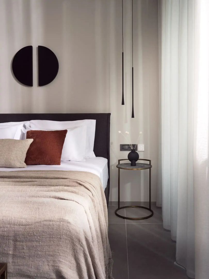 Doppelbett mit beigen und braunen Kissen, modernem Nachttisch und hängenden Leuchten.