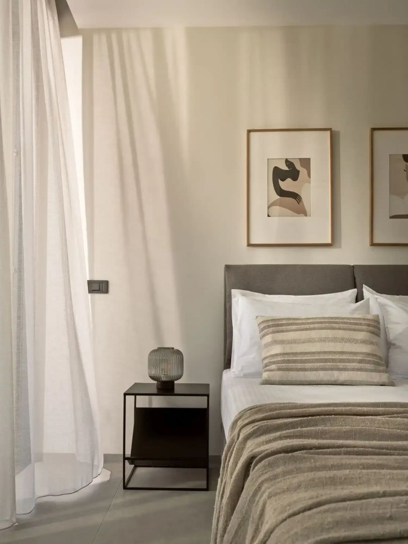 Helles Schlafzimmer mit gepolstertem Kopfteil, Bildern an der Wand und Vorhang.