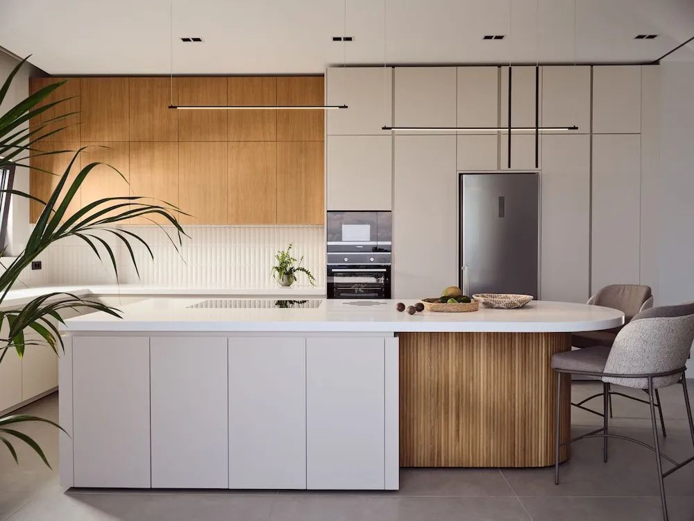 Moderne Küchenzeile mit hellen Schränken, Holzverkleidung und Edelstahlkühlschrank.
