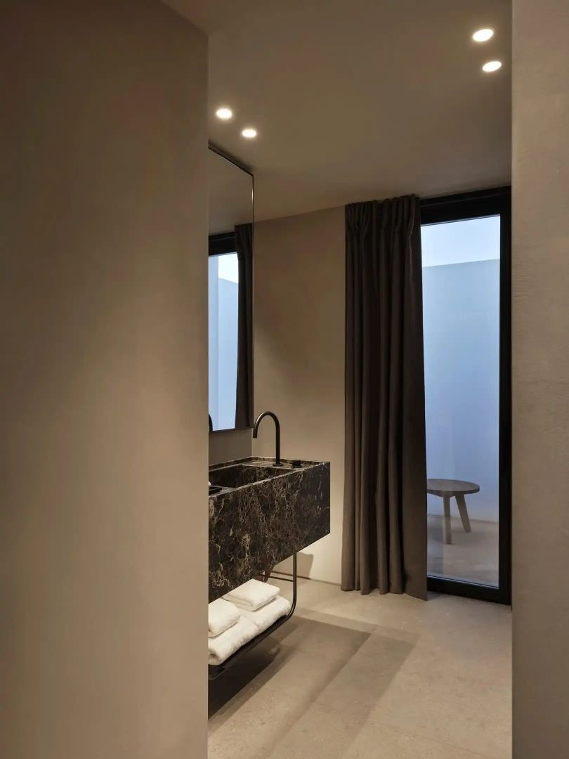 Badezimmer mit dunklem Marmorwaschtisch, schwarzer Armatur und Vorhang.