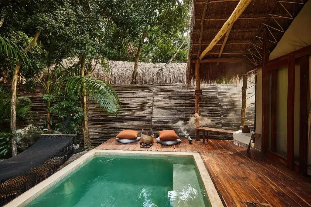 Kleines Schwimmbecken auf einer Holzterrasse umgeben von tropischen Pflanzen.