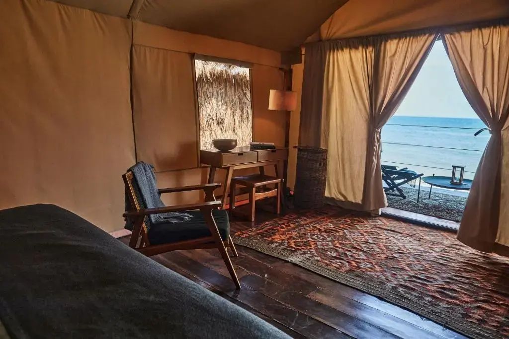 Einrichtung eines Zeltzimmers mit Holzsessel, Schreibtisch, Teppich und Blick auf das Meer.