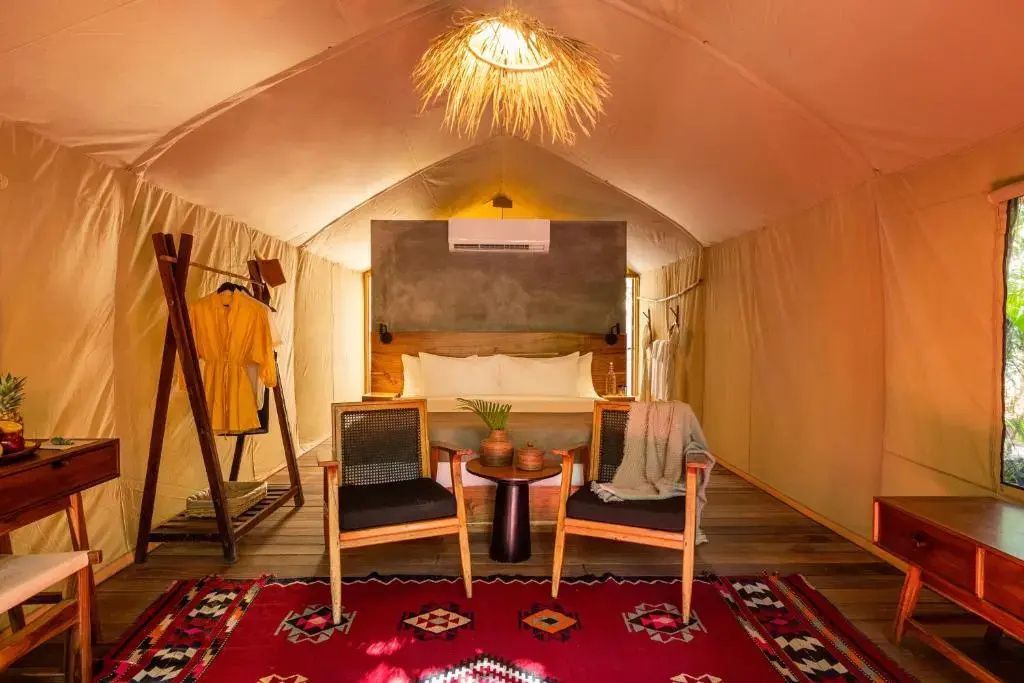 Geräumiges Zeltzimmer mit Doppelbett, zwei Holzsesseln, buntem Teppich und warmem Licht.