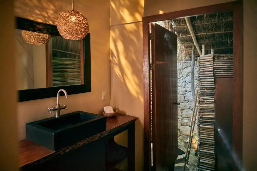 Badezimmer mit dunklem Waschtisch, Spiegel und Durchgang zur Außendusche.