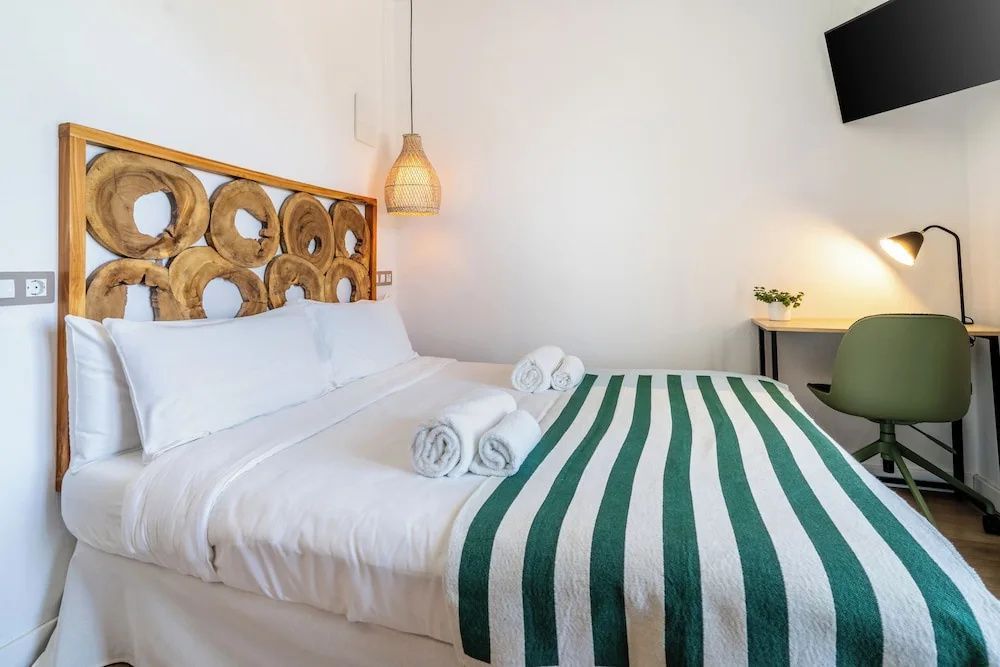 Doppelbett mit hölzernem Kopfteil, weißer Bettwäsche und grün gestreifter Tagesdecke.