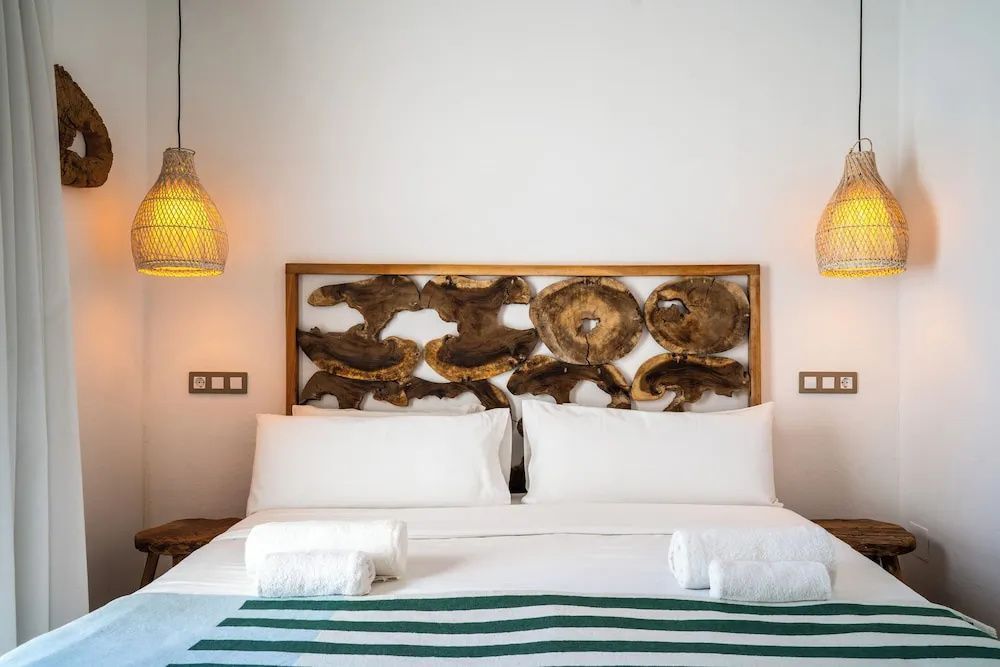 Doppelbett mit weißer Bettwäsche, gestreifter Decke und ein Kopfteil aus Holzscheiben.