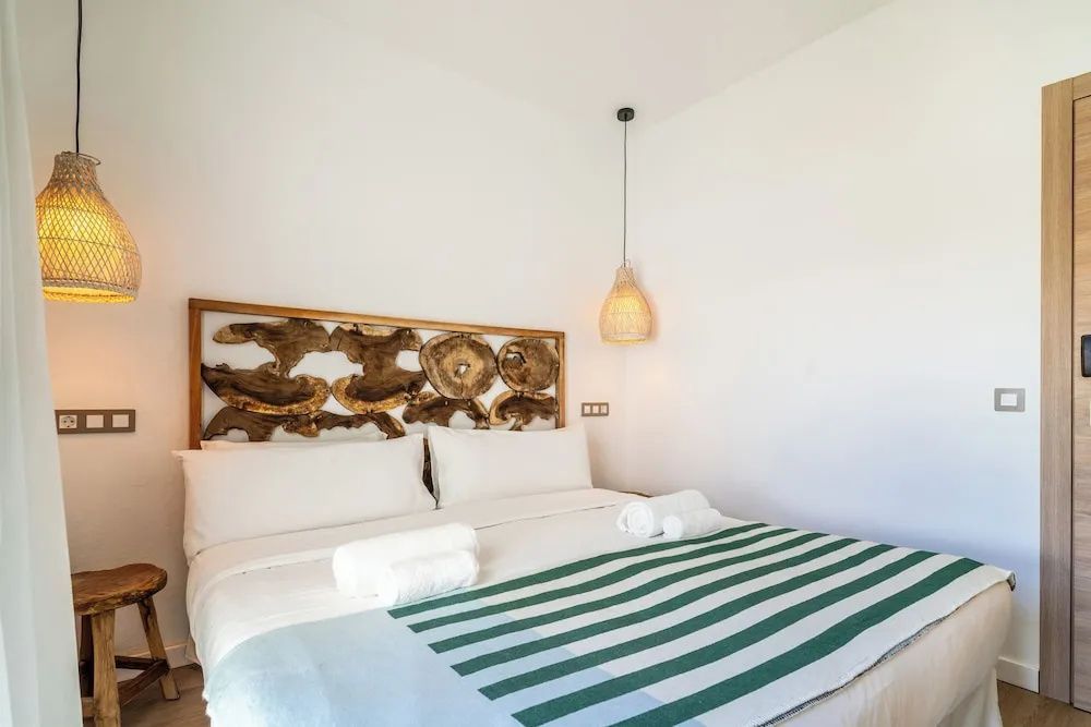 Helles Hotelzimmer mit Doppelbett, grün gestreifter Tagesdecke und einer hängenden Lampe.