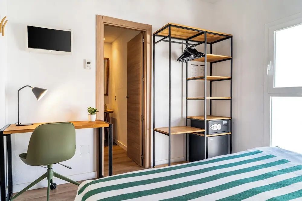 Blick im Zimmer auf ein offenes Kleiderregal aus Metall, ein Schreibtisch und die Badezimmertür.