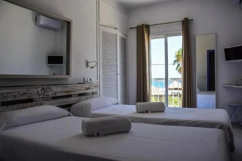 Schlafzimmer mit zwei weiß bezogenen Einzelbetten, weißem Schrank und Klimaanlage.
