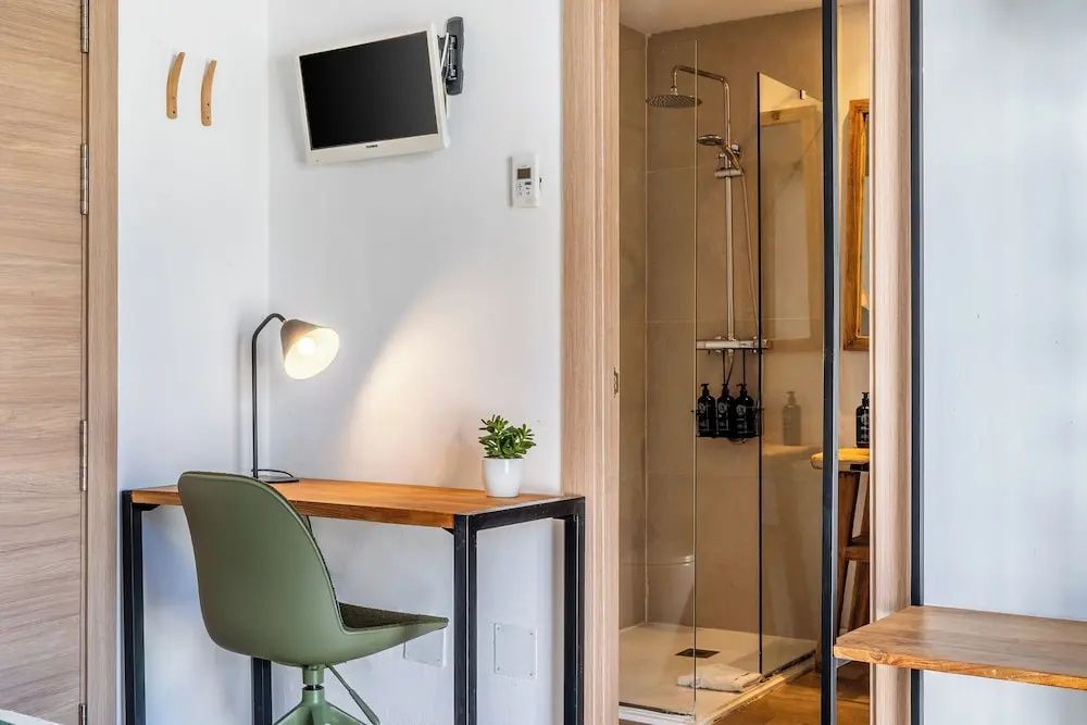 Schreibtisch mit grünem Stuhl, Schreibtischlampe und Blick auf das angrenzende Badezimmer.