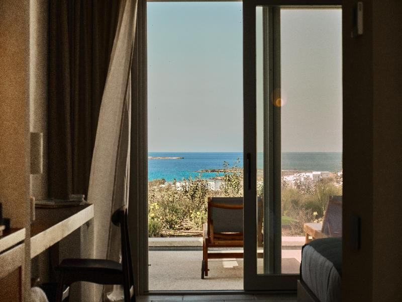 Blick durch eine geöffnete Glas-Schiebetür auf eine Terrasse mit Sonnenliege und Meer.