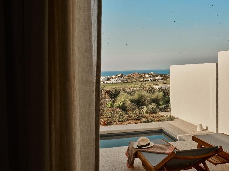 Blick am Vorhang vorbei auf eine Terrasse mit privatem Pool und Meer am Horizont.