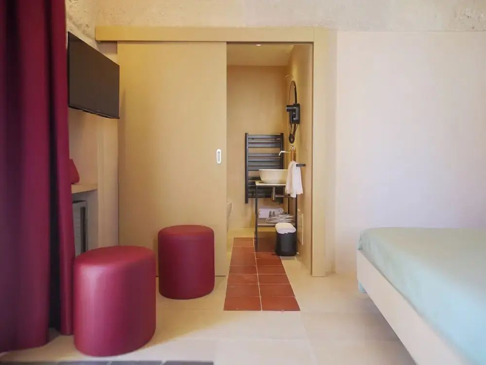 Hotelzimmer mit roten Hockern, Fernseher und Blick auf das angrenzende Badezimmer.