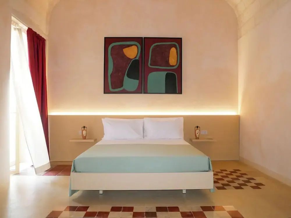 Doppelbett mit hellblauer Decke vor beigefarbener Wand und zwei Kunstwerken.