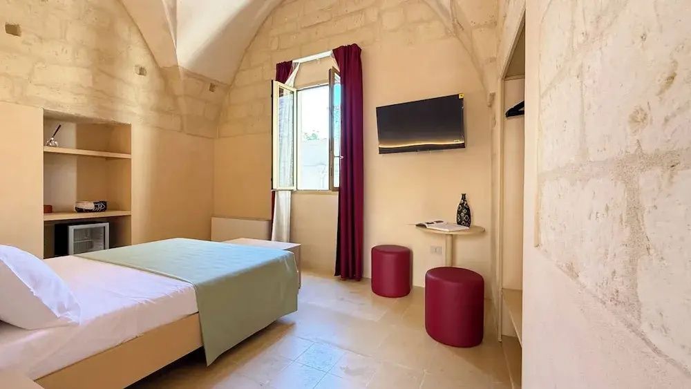 Schlafzimmer mit historischem Kreuzgewölbe, Doppelbett, Fernseher und rotem Vorhang.