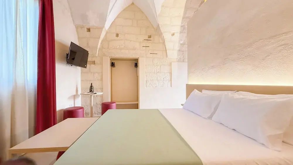 Blick auf ein helles Zimmer mit Natursteinwänden, Gewölbedecke und grossem Doppelbett.