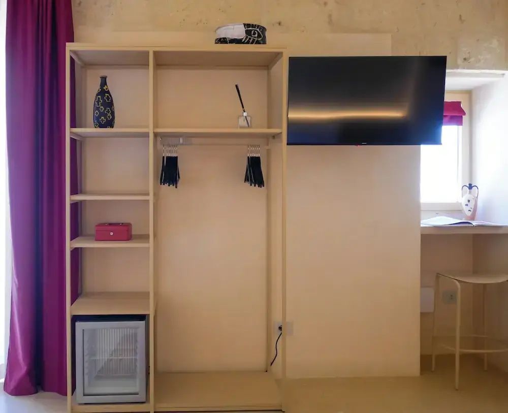 Offenes Holzregal mit Minibar und Kleiderbügeln neben einem Wandfernseher.