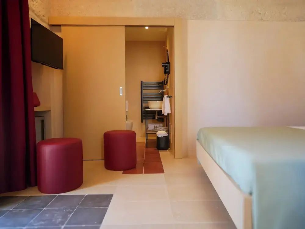 Helles Schlafzimmer mit zwei roten Sitzhockern, Holzschiebetür und Sicht ins Bad.