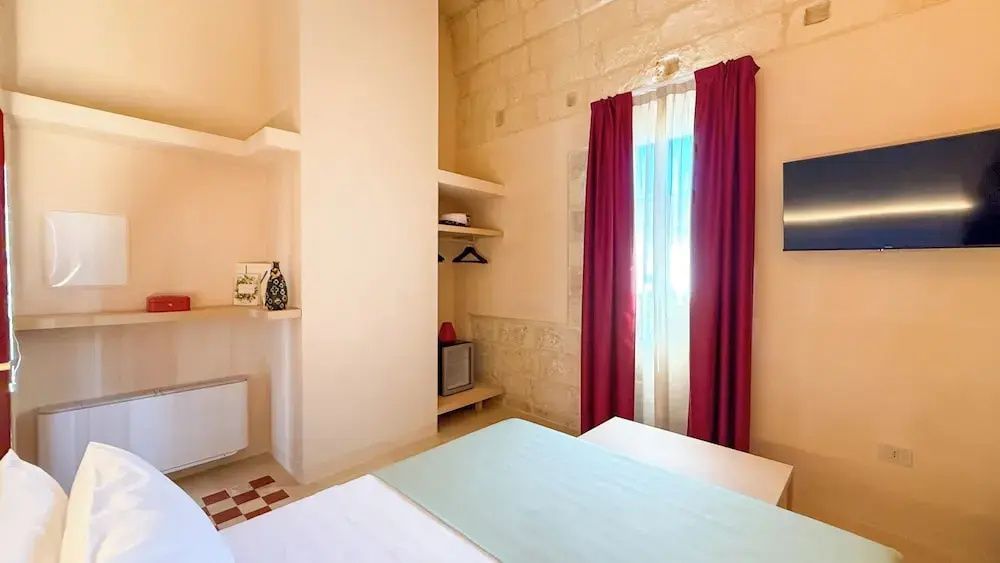 Helles Hotelzimmer mit Steinwand, rotem Vorhang und offenem Schrank.