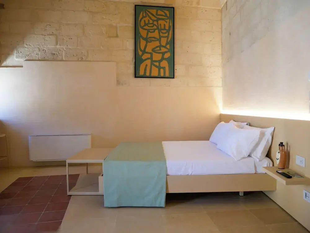Doppelbett mit hellgrüner Tagesdecke vor einer Natursteinwand mit grünem Kunstwerk.
