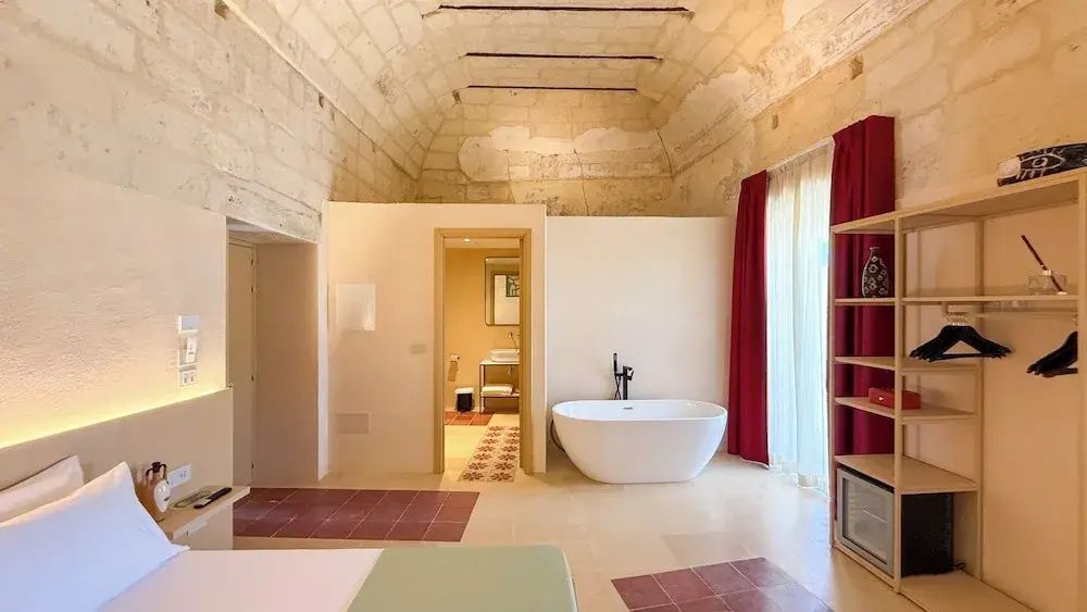 Zimmer mit historischem Gewölbe, freistehender Badewanne und Blick ins Badezimmer.