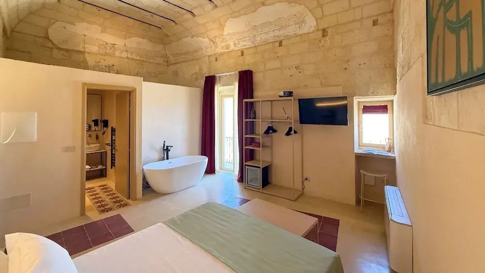 Zimmer mit historischem Steingewölbe, freistehender Badewanne und Fernseher.