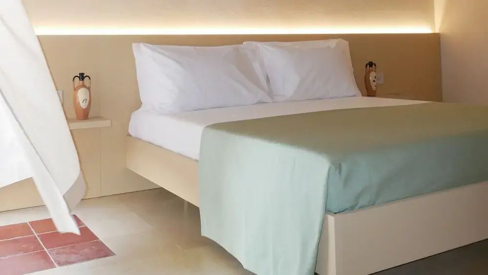 Doppelbett mit weißer Bettwäsche, hellgrüner Überdecke und beleuchtetem Kopfteil.