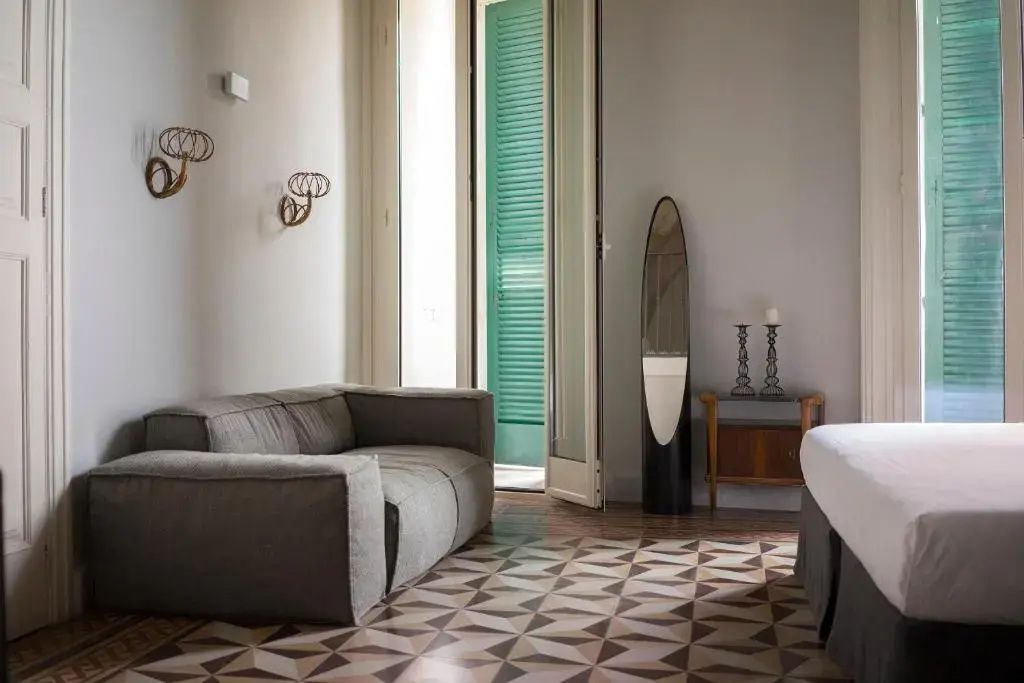 Sitzbereich im Zimmer mit grauem Sofa, ovalem Standspiegel und Tür zum Balkon.