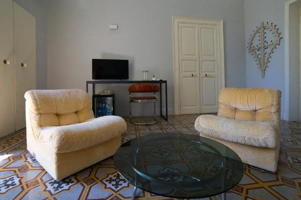 Zwei beige Sessel stehen um einen gläsernen Couchtisch auf einem gemusterten Fliesenboden.