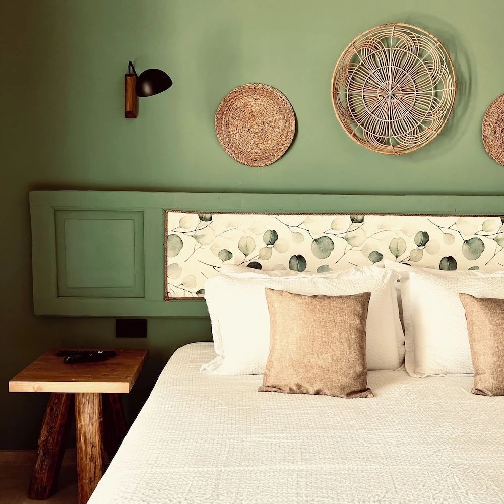 Doppelbett mit weißer Bettwäsche vor grüner Wand mit geflochtenen Wandtellern.