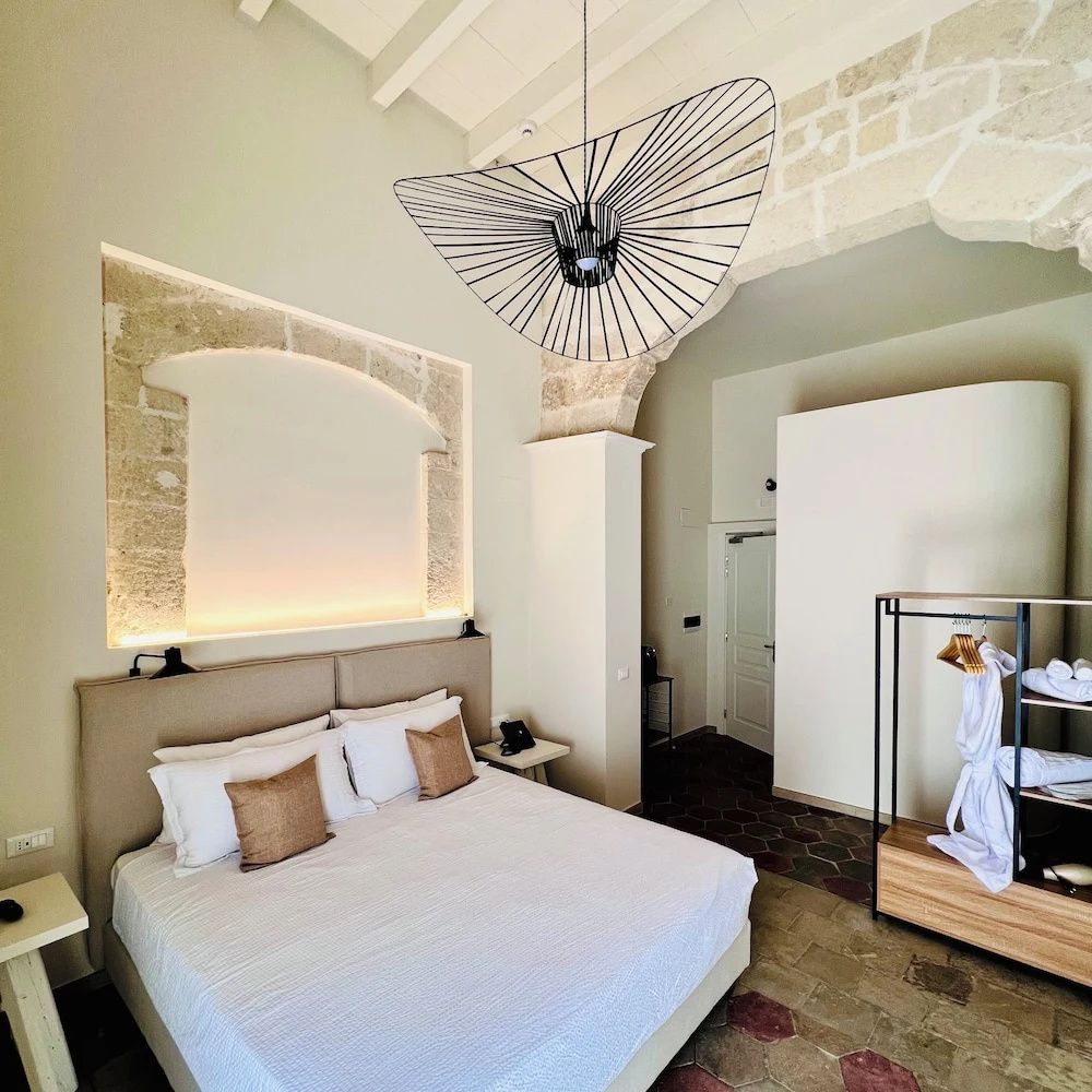 Geräumiges Hotelzimmer mit Doppelbett, Natursteinbogen an der Wand und moderner Hängeleuchte.