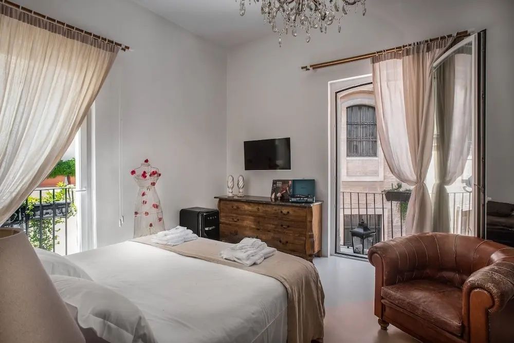 Helles Schlafzimmer mit Doppelbett, Holzkommode, Sessel und Blick durch das Fenster.