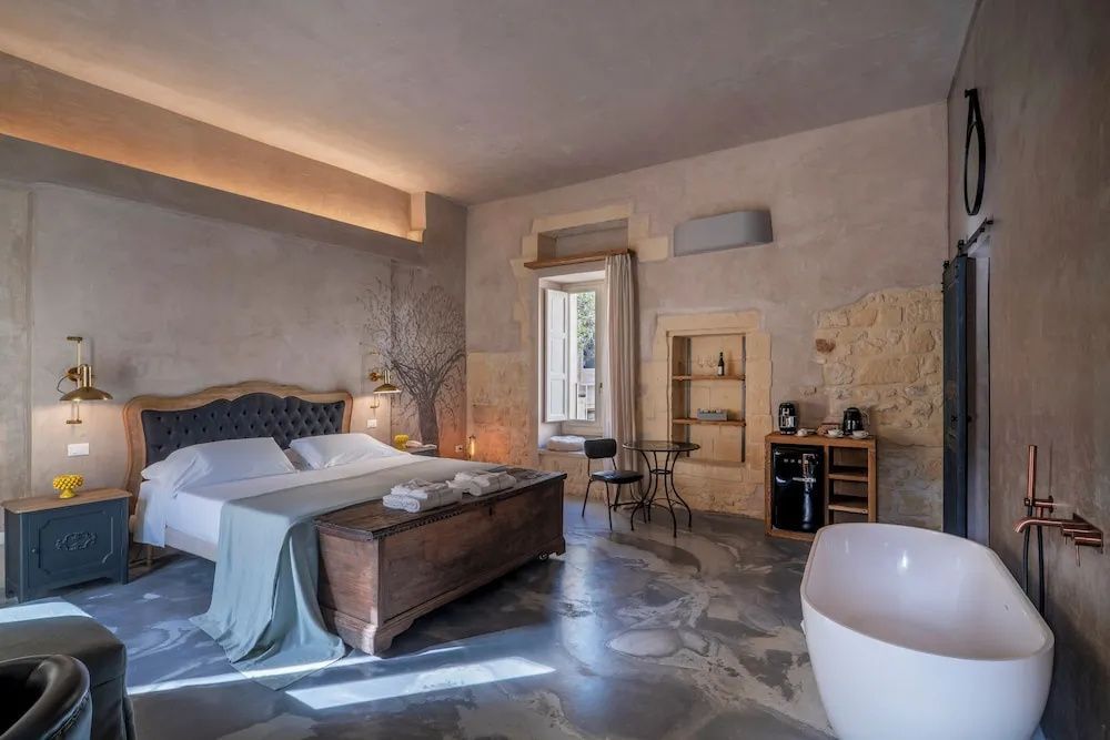 Geräumiges Hotelzimmer mit Doppelbett, Holztruhe, Esstisch und freistehender Badewanne.