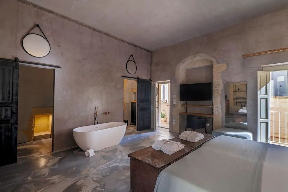 Hotelzimmer mit freistehender Badewanne, Flachbild-TV und verputzten Natursteinwänden.