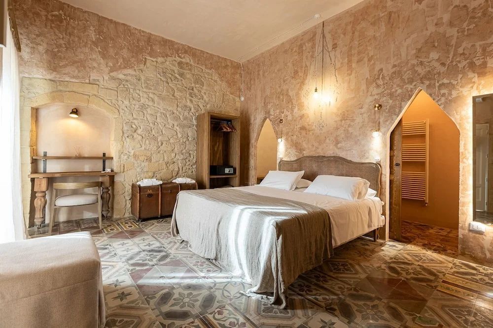 Schlafzimmer mit historischer Steinwand, gefliestem Boden und großem Doppelbett.