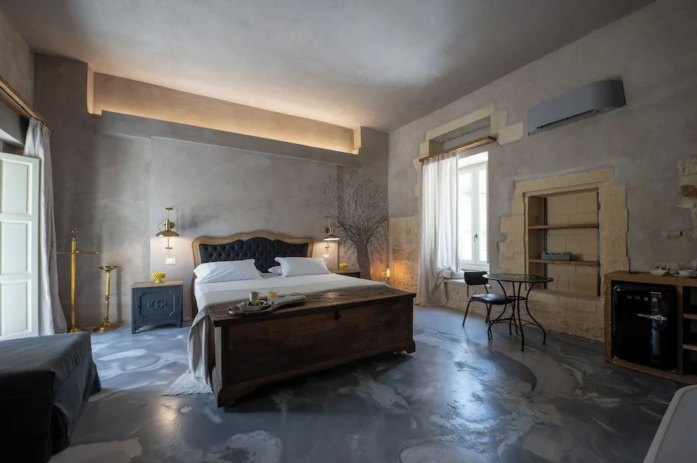 Geräumiges Hotelzimmer mit Doppelbett, Truhe aus Holz und hellen Verputzwänden.